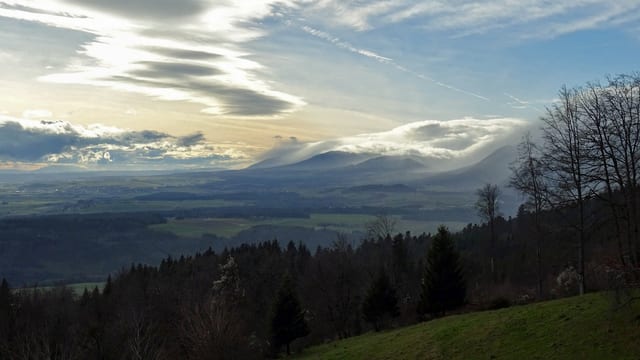 Blick über Wiesen und Wald auf Ebene und Berge mit blauem Himmel und Wolken. Blick über Wiesen und Wald auf Ebene und Berge mit blauem Himmel und Wolken.