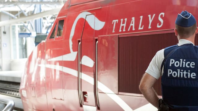 Ein belgischer Polizist steht vor einem roten Thalys-zug. Ein belgischer Polizist steht vor einem roten Thalys-zug.