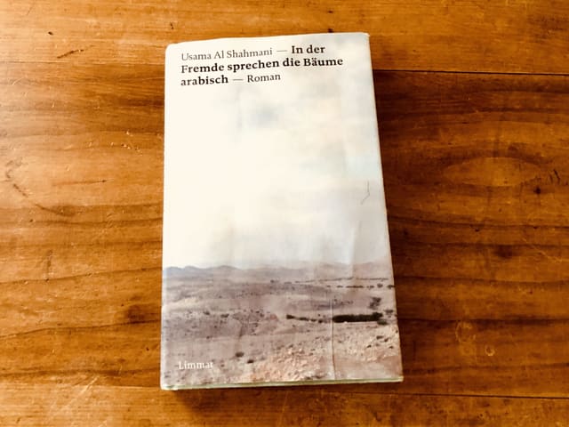 «In der Fremde sprechen die Bäume arabisch» von Usama Al Shahmani liegt auf einem blanken Holztisch «In der Fremde sprechen die Bäume arabisch» von Usama Al Shahmani liegt auf einem blanken Holztisch