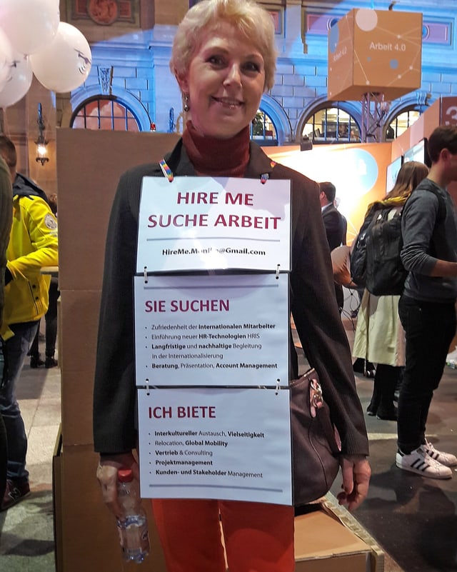 Eine ältere Dame steht am HB Zürich. Sie hat sich mit Schildern behängt, auf denen steht, dass sie eine Stelle sucht. Eine ältere Dame steht am HB Zürich. Sie hat sich mit Schildern behängt, auf denen steht, dass sie eine Stelle sucht.