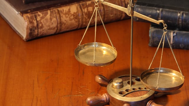 Eiine feine Waage vor dicken Justiz-Büchern Eiine feine Waage vor dicken Justiz-Büchern