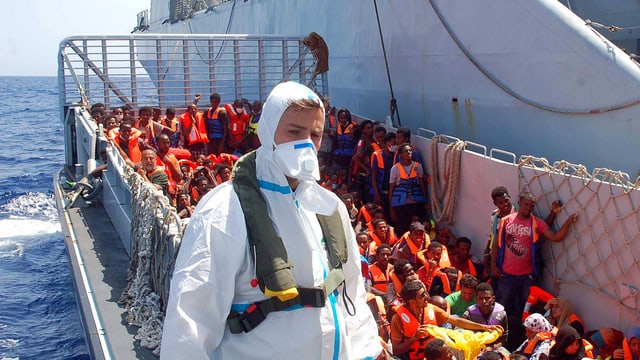 Mann in Schutzanzug mit Flüchtlingen Mann in Schutzanzug mit Flüchtlingen