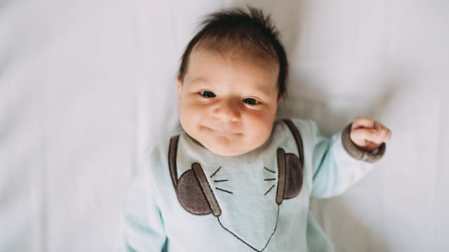 Symbolbild: Baby im Strampelanzug, es lächelt. Symbolbild: Baby im Strampelanzug, es lächelt.