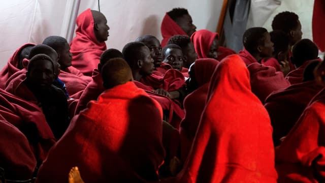 Migranten warten in Decken eingehüllt Migranten warten in Decken eingehüllt