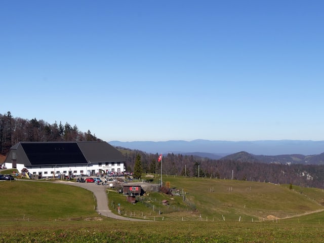 Links im Bild ein grosser Gutshof mit Festwirtschaft. Rechts Ausblick über sanfte Hügel und am Himmel keine einzige Wolke.