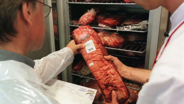Zwei Männer schauen auf ein vakumiertes Stück Fleisch. Im Hintergrund ein Kühlschrank. Zwei Männer schauen auf ein vakumiertes Stück Fleisch. Im Hintergrund ein Kühlschrank.