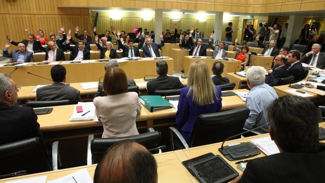 Ein heller Saal, in dem mehrere Politiker die Hände heben und abstimmen. Ein heller Saal, in dem mehrere Politiker die Hände heben und abstimmen.