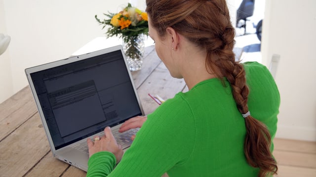 Eine Frau sitzt an einem Tisch und arbeitet an einem Notebook. Eine Frau sitzt an einem Tisch und arbeitet an einem Notebook.