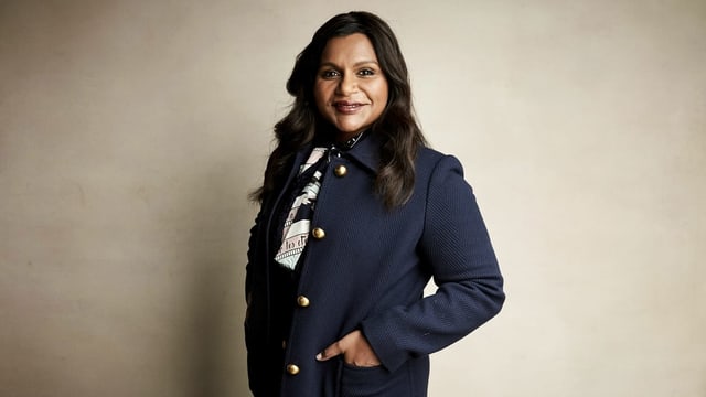 Mindy Kaling post für ein Foto vor einer grau-braunen Wand. Mindy Kaling post für ein Foto vor einer grau-braunen Wand.