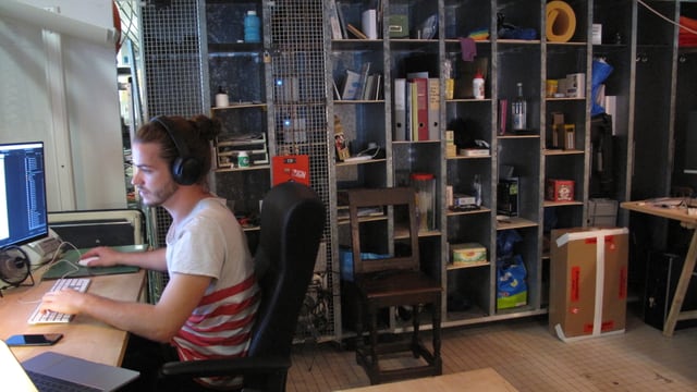 Ein Mann arbeitet am Computer im Hintergrund ein Büchergestell Ein Mann arbeitet am Computer im Hintergrund ein Büchergestell