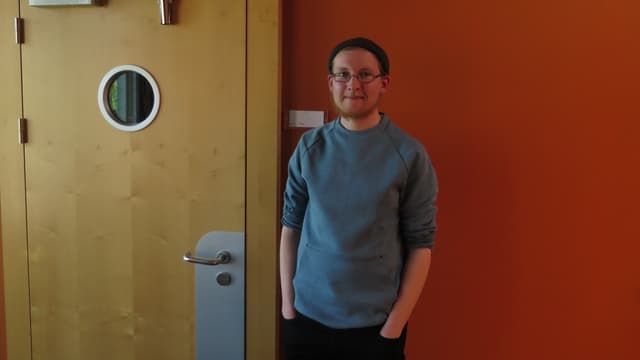 Junger Mann mit grauem Pullover, schwarzer Mütze und Brille Junger Mann mit grauem Pullover, schwarzer Mütze und Brille