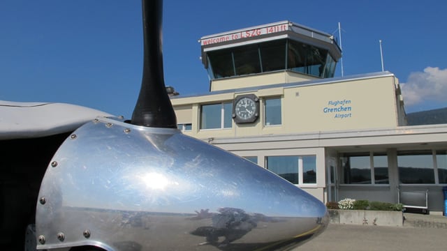 Flugzeugpropeller im Vordergrund, Flughafentower im Hintergrund. 