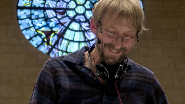 Mann mit Kopfhörern vor Kirchenfenster Mann mit Kopfhörern vor Kirchenfenster