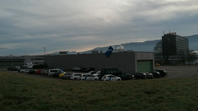 Blick auf die Halle der Busbetriebe Olten-Gösgen-Gäu, eine graue Halle mit Autoparkplätzen rundherum. Blick auf die Halle der Busbetriebe Olten-Gösgen-Gäu, eine graue Halle mit Autoparkplätzen rundherum.