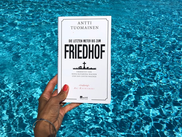 Annette König hält das Buch von Antti Tuomainen: «Die letzten Meter bis zum Friedhof» vor blaues Wasser Annette König hält das Buch von Antti Tuomainen: «Die letzten Meter bis zum Friedhof» vor blaues Wasser