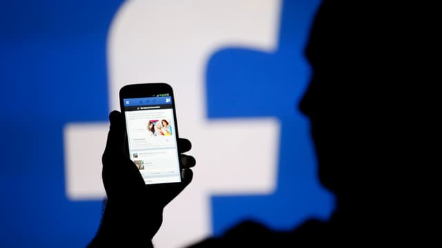 Ein Mann schaut auf ein Smartphone. Im Hintergrund ist ein Logo von «Facebook». Ein Mann schaut auf ein Smartphone. Im Hintergrund ist ein Logo von «Facebook».