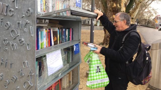 Mann mit Rucksack und Bücher in der Hand hebt Tür eines Regals auf. Mann mit Rucksack und Bücher in der Hand hebt Tür eines Regals auf.