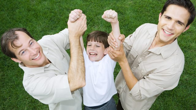 Zwei Männer halten ein Kind in die Höhe. Zwei Männer halten ein Kind in die Höhe.