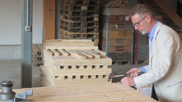 Mann in beigem Jacket hält Hammer über Holzpallett. Mann in beigem Jacket hält Hammer über Holzpallett.