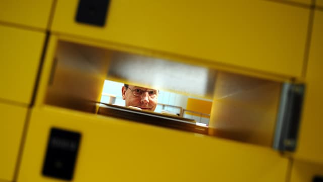Blick durch ein Postfach hindurch, dahinter ein Pöstler. Blick durch ein Postfach hindurch, dahinter ein Pöstler.