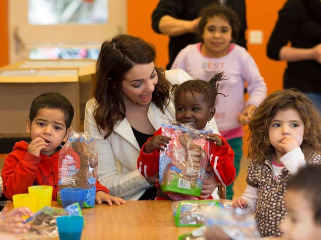 Laetitia Guarino an einem Tisch sitzend und von Kindern umgeben. Laetitia Guarino an einem Tisch sitzend und von Kindern umgeben.