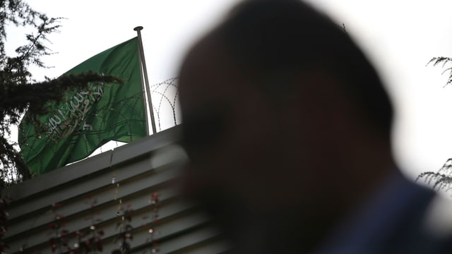 Silhouette eines Mannes vor einem Gebäude. Darauf weht die Flagge Saudi-Arabiens. Silhouette eines Mannes vor einem Gebäude. Darauf weht die Flagge Saudi-Arabiens.