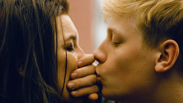 Ein Junge hält seine Hand auf den Mund einer Frau. Er küsst die Hand.