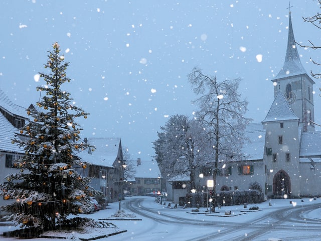 Dorfplatz mit verschneitem Weihnachtsbaum und Kirche