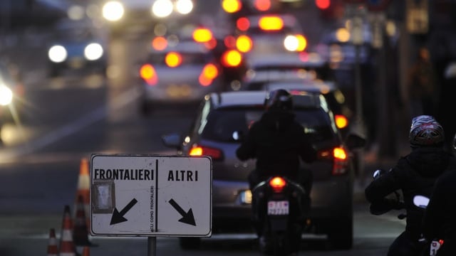 An der Grenze. Autos und Motos stehen Schlange. Auf einem Schild steht frontalieri und altri. Es ist abends. An der Grenze. Autos und Motos stehen Schlange. Auf einem Schild steht frontalieri und altri. Es ist abends.