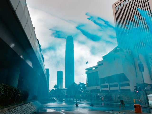 Blau gefärbtes Wasser spritzt in hohem Bogen über eine Strasse Blau gefärbtes Wasser spritzt in hohem Bogen über eine Strasse