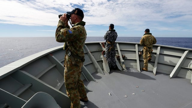 Drei Soldaten blicken vom Bug eines Militärschiffes mit Feldstechern hinaus aufs Meer. Drei Soldaten blicken vom Bug eines Militärschiffes mit Feldstechern hinaus aufs Meer.