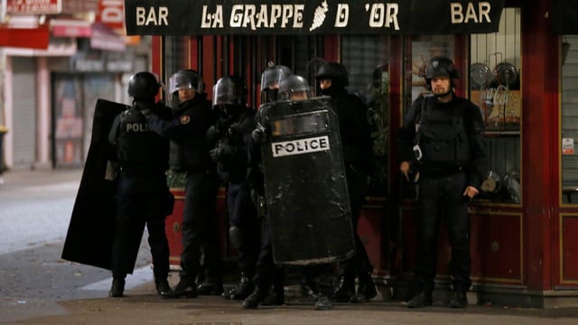 Mehrere Polizisten in Schutzmontur vor einer Bar. Mehrere Polizisten in Schutzmontur vor einer Bar.