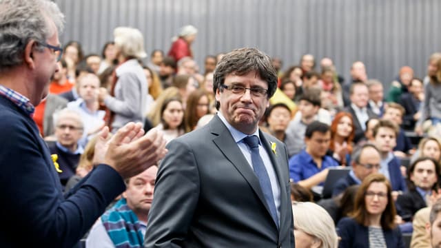 Puigdemont steht inmitten von sitzenden Zuhörenden. Einer von ihnen steht und klatscht dem Separatistenführer zu. Puigdemont steht inmitten von sitzenden Zuhörenden. Einer von ihnen steht und klatscht dem Separatistenführer zu.