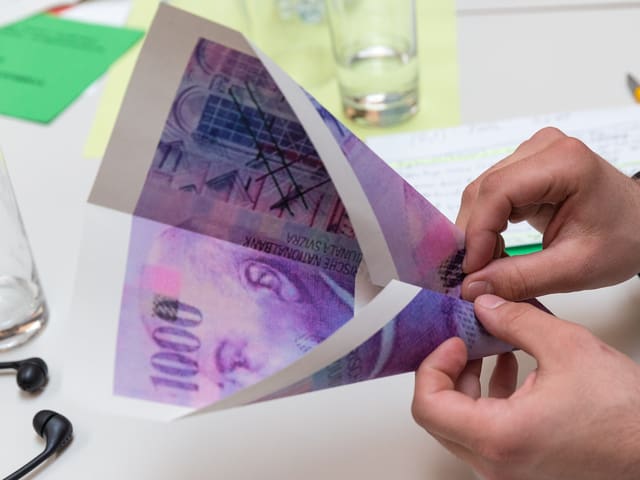 Ein Delegierter bastelt ein Papierflugzeug aus einer Kopie der Tausender-Note. Ein Delegierter bastelt ein Papierflugzeug aus einer Kopie der Tausender-Note.