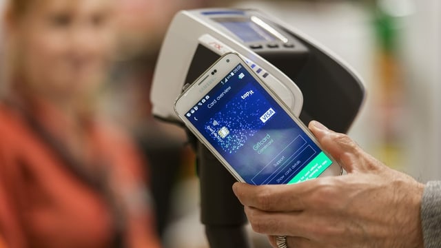 Hand hält Handy an Gerät. Hand hält Handy an Gerät.