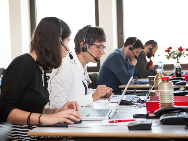 Vier Menschen sitzen am Telefon.