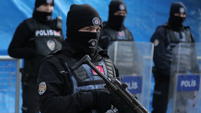 Schwer bewaffnete Polizisten in Schwarz stehen in einer Reihe, einer im Vordergrund. Schwer bewaffnete Polizisten in Schwarz stehen in einer Reihe, einer im Vordergrund.