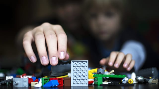 Eine Erwachsenen- und eine Kinderhand greifen nach Legobauklötzen. Eine Erwachsenen- und eine Kinderhand greifen nach Legobauklötzen.