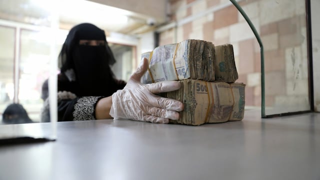 Eine verschleierte Frau bündelt Banknoten. Eine verschleierte Frau bündelt Banknoten.