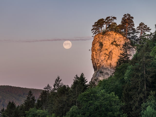 Ein Fels im Morgenrot, dahinter der Vollmond.