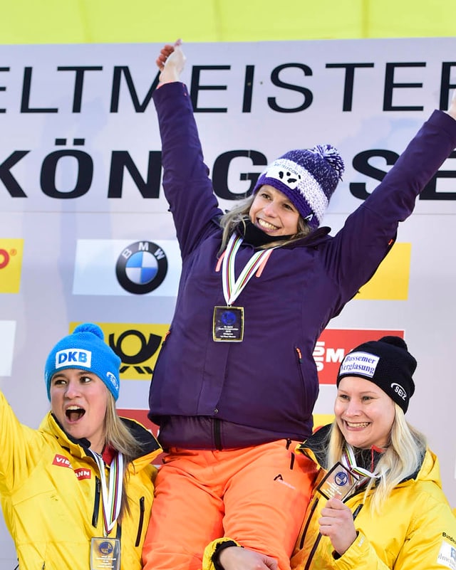 Martina Kocher auf dem Podest zusammen mit Natalie Geisenberger und Dajana Eitberger, die die Siegerin hochheben. Martina Kocher auf dem Podest zusammen mit Natalie Geisenberger und Dajana Eitberger, die die Siegerin hochheben.