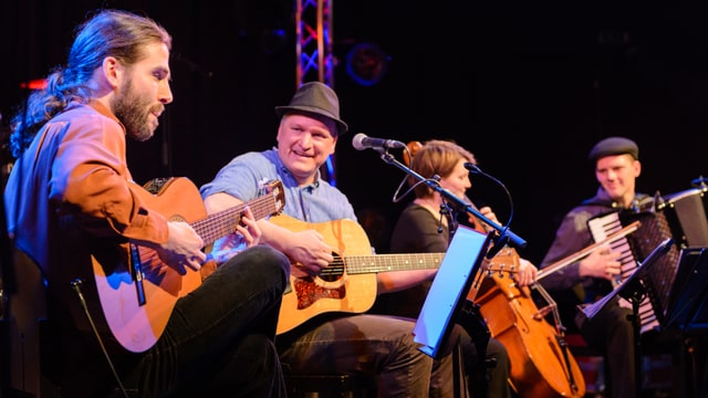 Vier Musiker mit Gitarren, Cello und Akkordeon auf einer Bühne. Vier Musiker mit Gitarren, Cello und Akkordeon auf einer Bühne.