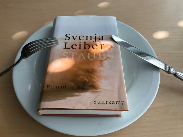 Der Roman «Staub» liegt auf einem weissen Teller. Messer und Gabel sind angelehnt. Der Roman «Staub» liegt auf einem weissen Teller. Messer und Gabel sind angelehnt.