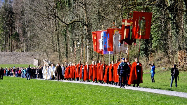 Die Fahnenträger sind mit roten Umhängen an der Prozession unterwegs. Die Fahnenträger sind mit roten Umhängen an der Prozession unterwegs.