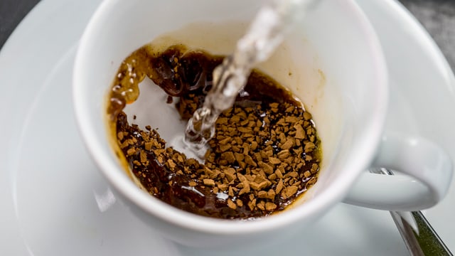 Löslicher Nescafé in einer Tasse. Heisses Wasser wird hinzugeschüttet. Löslicher Nescafé in einer Tasse. Heisses Wasser wird hinzugeschüttet.