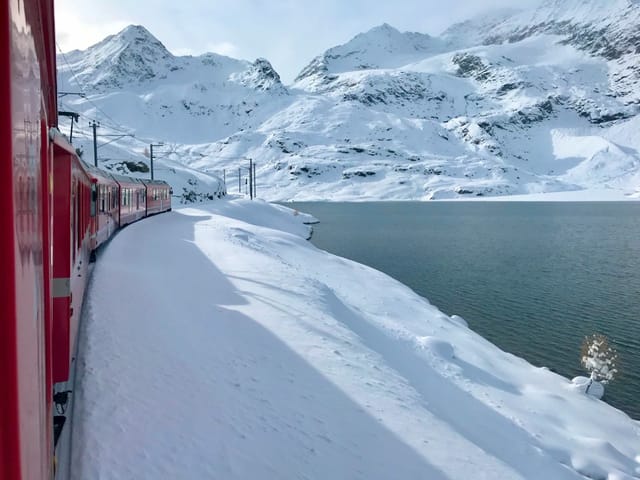Blick aus einem Zugfenster auf den Schnee und einen See.
