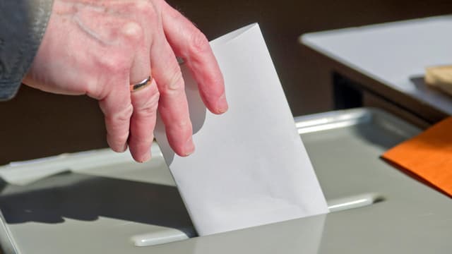 Hand wirft Wahlzettel in eine Urne Hand wirft Wahlzettel in eine Urne