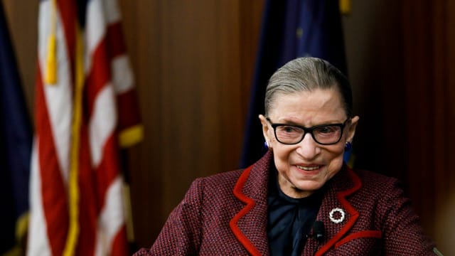 Ruth Bader-Ginsberg lächelt vor der US-Flagge Ruth Bader-Ginsberg lächelt vor der US-Flagge