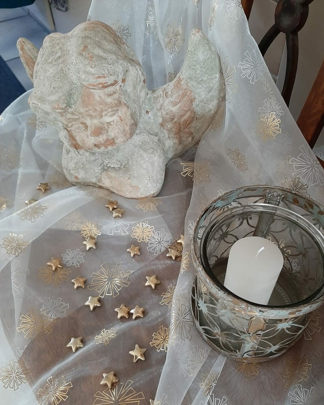 Tönerner Engel auf Chiffontuch und Kerze.