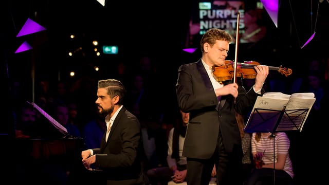 Ein Mann spielt Violine auf der Bühne, daneben ein weiterer Piano. Ein Mann spielt Violine auf der Bühne, daneben ein weiterer Piano.